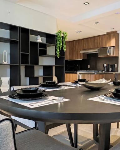 Round dining table set for seven with kitchen visible behind, in a Roma Norte apartment